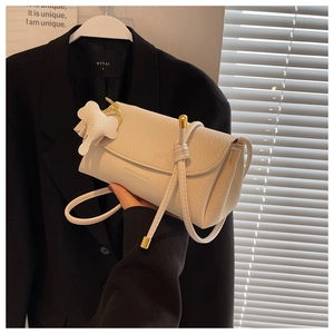 Detail of white textured leather shoulder bag featuring elephant charm and golden hardware