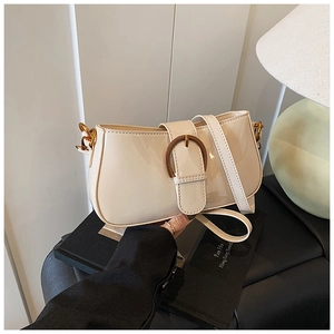 Gros plan du sac baguette en cuir verni crème avec boucle fer à cheval dorée