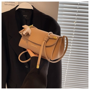 Detail of khaki pebbled leather bag featuring knotted shoulder strap and elephant charm