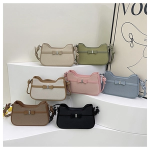 Detail of trendy small square bags with metal bow accent and textured shoulder strap
