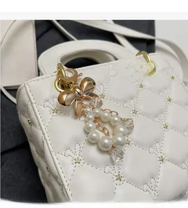 Détail d'un sac à main blanc matelassé avec clous dorés et breloque noeud en perles
