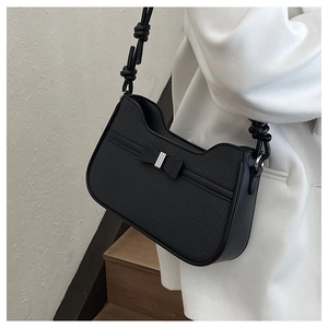 Detail of black woven crescent bag featuring a bow and knotted shoulder strap