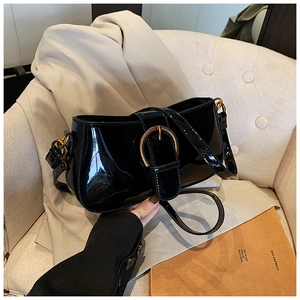 Détail du sac sous l'aisselle en cuir verni noir avec boucle dorée sur canapé
