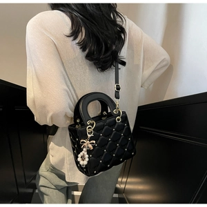 Gros plan du sac à main matelassé noir avec finition brillante et charme perle
