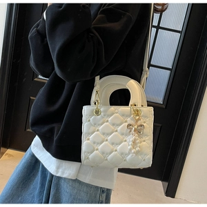 Détail du sac à bandoulière blanc matelassé en cœurs avec breloque nœud en perles et poignée