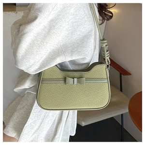 Detail of light green straw shoulder bag featuring a woven texture and bow decoration