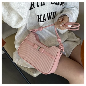 Close-up of pink woven bag with bow detail and knotted strap on a model shoulder