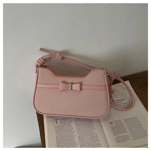 Detail of pink woven leather shoulder bag with decorative bow on artistic magazine