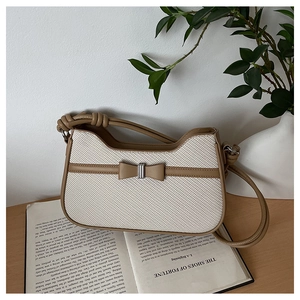 Detail of woven straw handbag with brown leather trim and bow on wooden desk