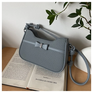 Detail of blue textured leather shoulder bag with bow and knotted handle on book