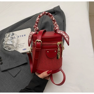 Detail of red bucket bag with woven straw base and decorative silk scarf handle wrap