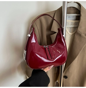Detail of burgundy patent leather crescent bag with glossy finish and silver buckle