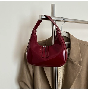 Detail of burgundy glossy crescent bag hanging next to a khaki blazer on a rack