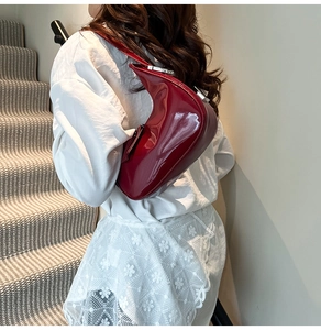 Close-up of a burgundy patent leather crescent bag worn by a model in a modern interior
