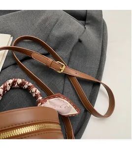 Detail of adjustable leather strap and silk scarf handle on brown bucket bag