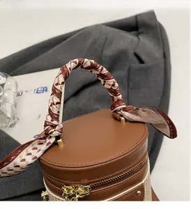 Detail of a brown bucket bag with a silk scarf handle and gold hardware on a grey blazer