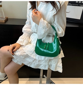 Green patent leather crescent bag worn by a model in a white dress for a stylish look