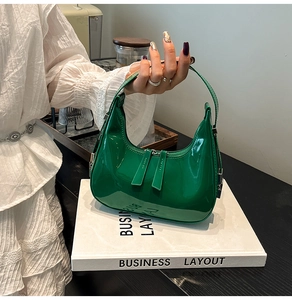 Detail of emerald green patent leather crescent bag with silver zipper and glossy finish