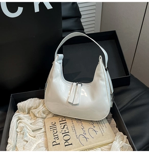 Detail of white glossy patent leather hobo bag inside a black gift box with book