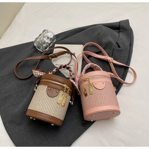 Detail of woven straw bucket bag with silk scarf handle and leather trim on grey fabric