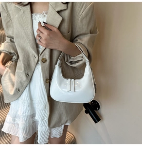 Close-up of white patent leather crescent bag styled with a beige blazer and lace dress