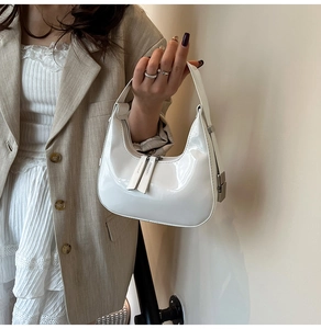 Close-up of glossy white patent leather crescent bag with dual metal zipper hardware