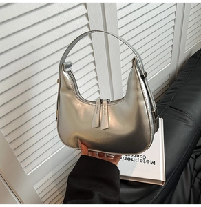 Close-up of a silver metallic crescent hobo bag held by hand in a minimalist setting