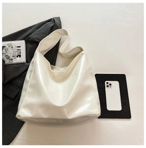 Top view of large white bucket bag with PU leather and wide strap on dark office background