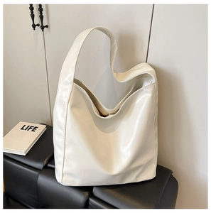 Detail of white soft leather bucket bag with magnetic clasp and wide strap on black bench