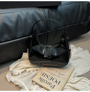 Detail of black patent leather crescent hobo bag with dual zippers on lace background