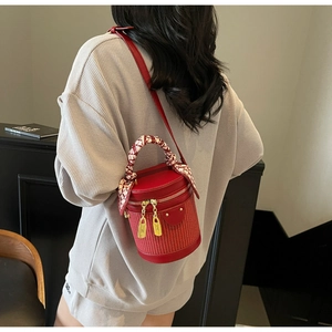 Detail of red bucket bag with woven texture, golden lock charms and silk scarf wrap