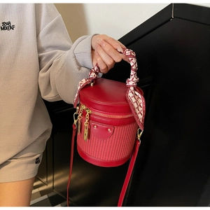 Detail of red cylindrical bucket bag with silk scarf handle and golden hardware