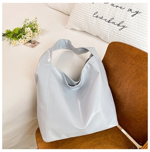 Detail of light grey glossy leather hobo bag with wide shoulder strap on a wooden chair