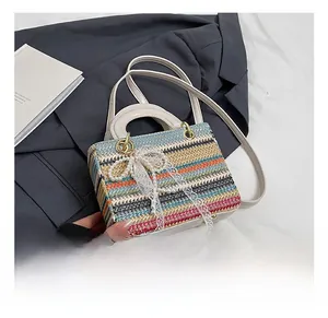 Détail du sac en paille à rayures colorées avec nœud en dentelle perlée et lanière blanche