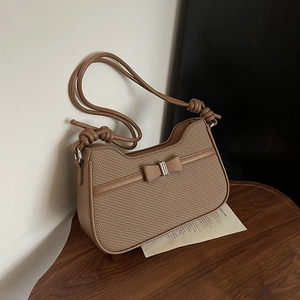 Brown woven fabric and leather shoulder bag with bow buckle on wooden table