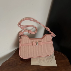 Pink woven leather handbag with bow detail and knotted shoulder strap in a minimalist setting