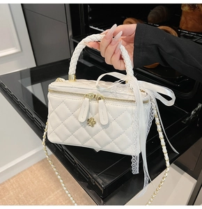Close-up of white quilted leather vanity bag with woven handle and lace bow detail