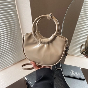 Minimalist beige saddle bag with glossy finish and metal ring handle in mirror reflection