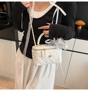 Detail of white quilted crossbody bag with golden flower clasp and chain strap