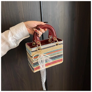 Détail d'un sac à main tissé multicolore avec poignées en cuir verni rouge et nœud perlé