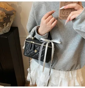 Detail of black quilted leather crossbody bag with white lace trim and gold flower logo