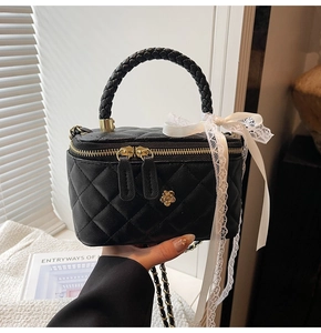 Detail of black quilted crossbody bag featuring gold flower accent and lace bow handle