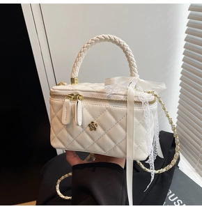 Detail of white quilted handbag featuring a gold camellia ornament and lace bow handle