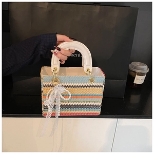 Détail d'un sac à main tressé multicolore avec poignée blanche et breloque perle et nœud