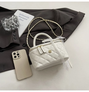 Detail of white quilted box bag with floral metal clasp, lace ribbon and gold chain strap