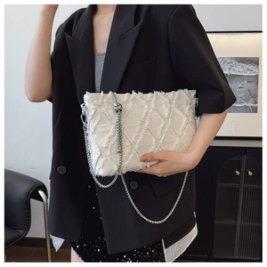 Detail of cream quilted denim bag with frayed edges and silver chain strap on a model