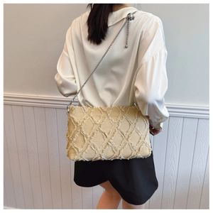 Detail of beige quilted crossbody bag with frayed fringe texture and slim metal chain