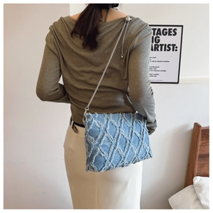 Detail of blue denim crossbody bag with quilted texture and chain strap on a model