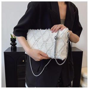 Macro view of white frayed denim bag with diamond quilting and silver metal chain