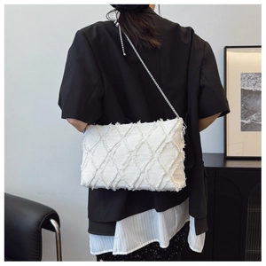Detail of white quilted denim crossbody bag with fringe texture and silver chain strap